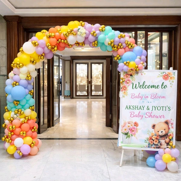 Colorful pastel rainbow balloon arch entrance decoration with a 'Baby in Bloom' teddy bear welcome signboard in Jaipur by Shava Moments.