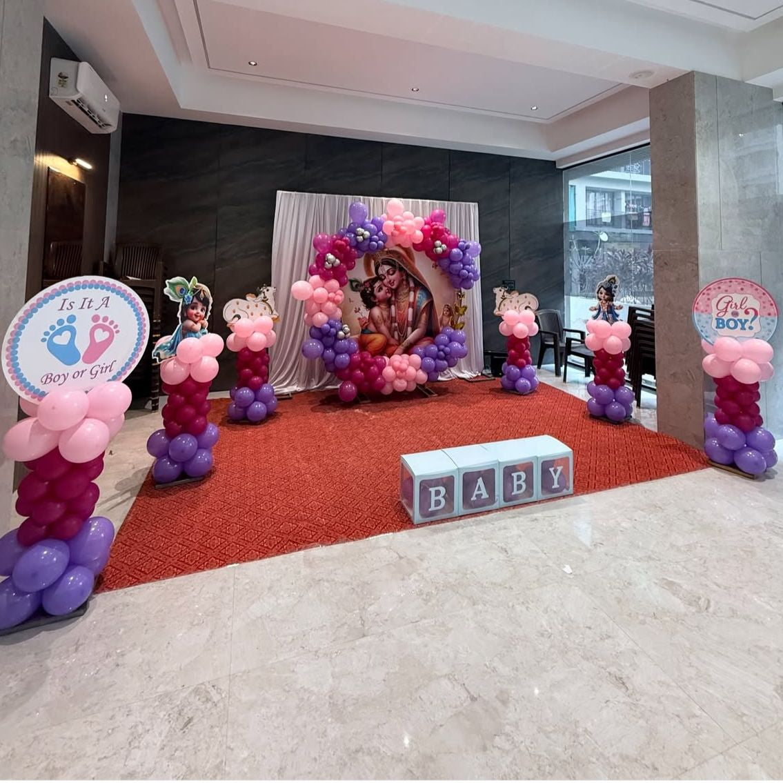 Grand baby shower stage setup in Jaipur featuring a circular God blessing backdrop, pink and purple balloon pillars, and gender reveal signs by Shava Moments.