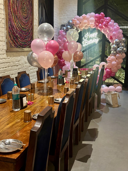 Intimate birthday dinner setup in Jaipur by Shava Moments, featuring a pink and silver balloon arch, neon Happy Birthday sign, and elegant table decorations with rose petals
