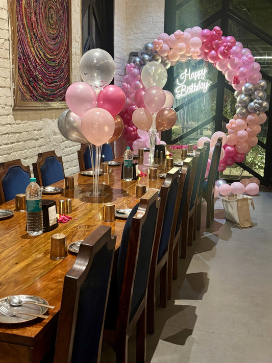 Intimate birthday dinner setup in Jaipur by Shava Moments, featuring a pink and silver balloon arch, neon Happy Birthday sign, and elegant table decorations with rose petals