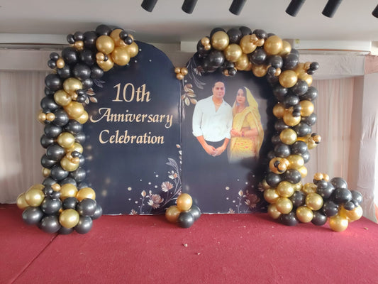 Elegant Wedding anniversary stage decoration in Jaipur featuring a customized photo backdrop and black and gold balloon garland by Shava Moments.