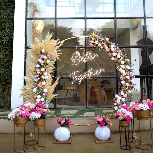 Minimalist circular gold ring backdrop in Jaipur with pampas grass, pink roses, and a Better Together neon sign by Shava Moments.