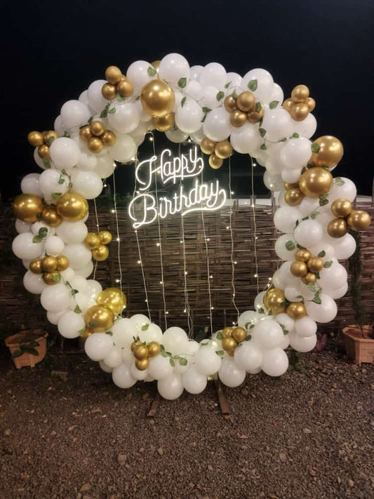 Sophisticated white and metallic gold circular balloon arch with a Happy Birthday neon sign in Jaipur by Shava Moments.