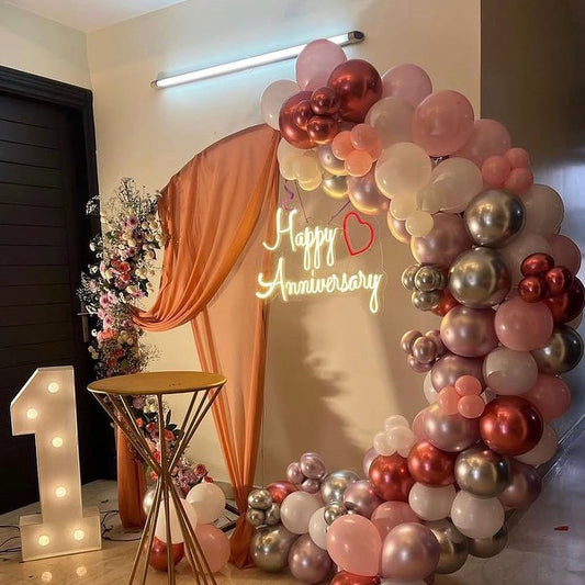 Home anniversary decor in Jaipur featuring a rose gold balloon arch, neon sign, fabric drapery, and marquee number 1 by Shava Moments.
