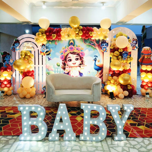 Outdoor traditional baby shower stage in Jaipur featuring a large Bal Krishna backdrop, balloon arches, and lighted marquee BABY letters by Shava Moments.