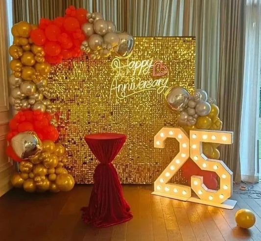 Gold sequin shimmer wall 25th anniversary backdrop in Jaipur with orange, chrome silver, and gold balloons by Shava Moments.