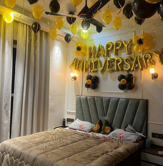 Romantic bedroom anniversary decoration in Jaipur featuring gold foil letter balloons, hanging ceiling balloons, and black balloon flowers.