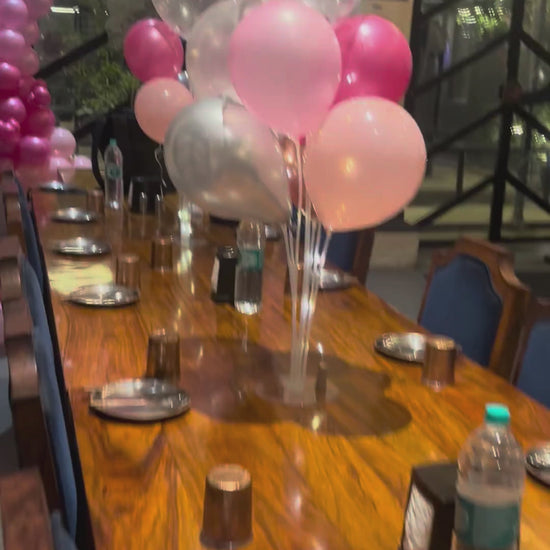 A behind-the-scenes look at Shava Moments decorators setting up a birthday dinner in Jaipur, showing the installation of a pink balloon arch, neon signage, and table centerpiece balloons