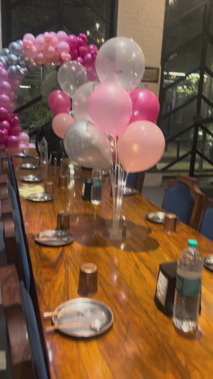 A behind-the-scenes look at Shava Moments decorators setting up a birthday dinner in Jaipur, showing the installation of a pink balloon arch, neon signage, and table centerpiece balloons